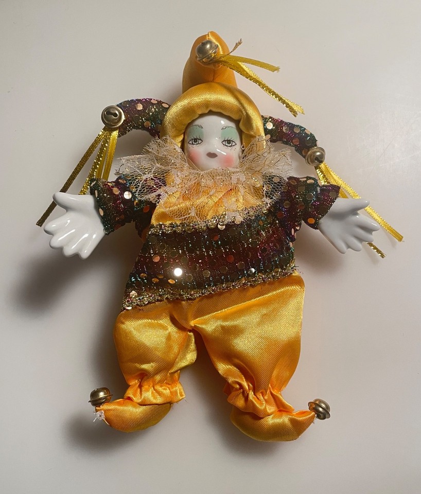 a porcelain faced softbody clown wearing a shiny yellow outfit lays with hands outstretched as if to beckon in good fortune