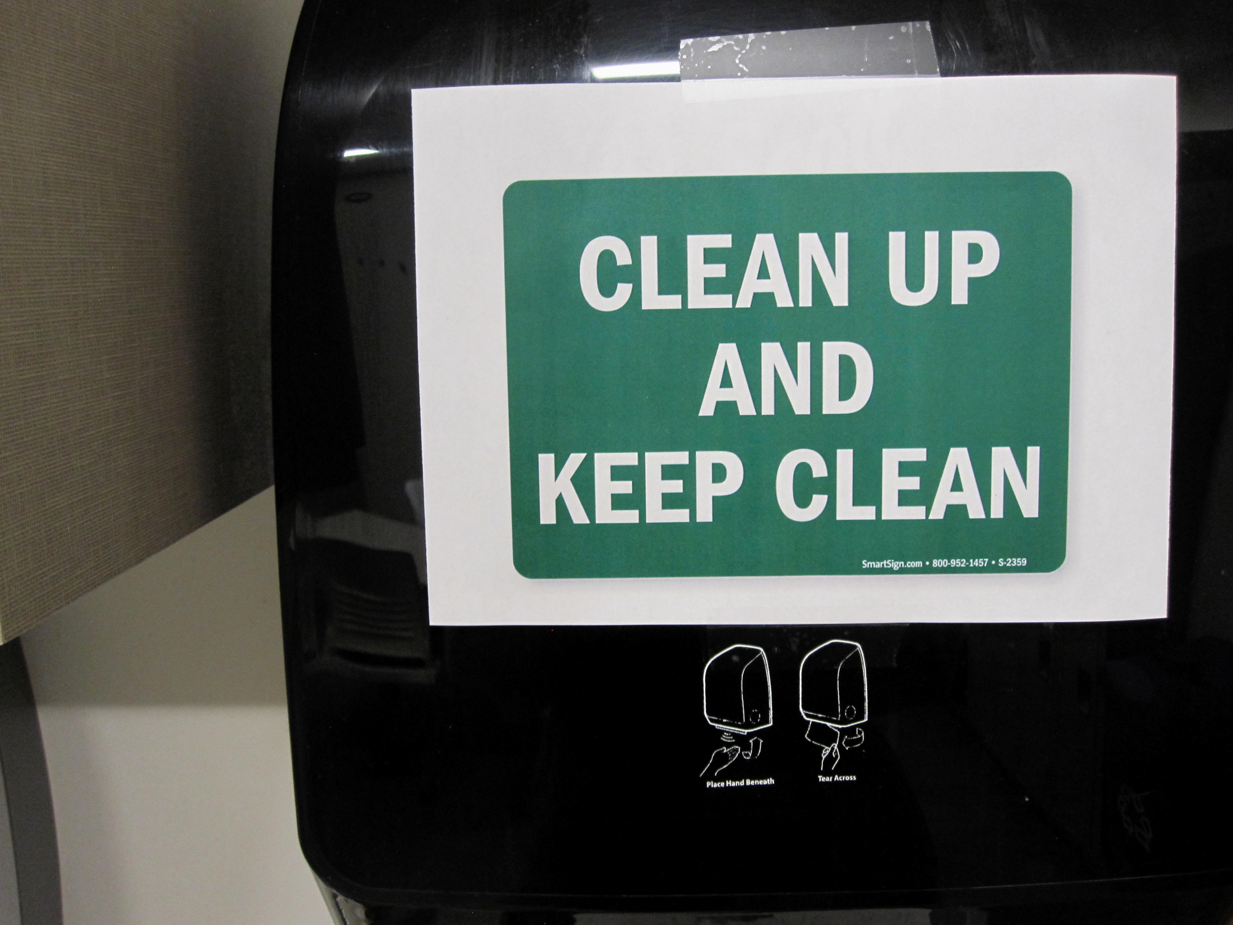 a passive aggressive sign encouraging viewers to clean up, taped to a hand towel dispenser
