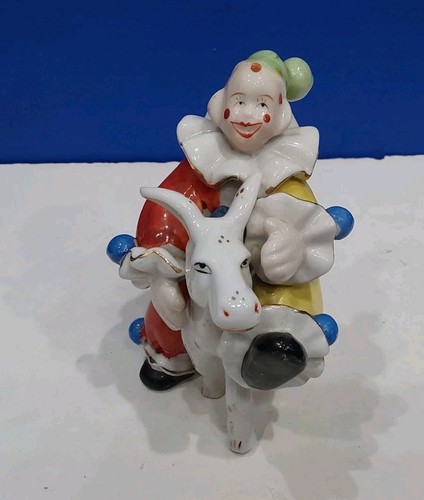 a porcelain clown in red and yellow rides a donkey