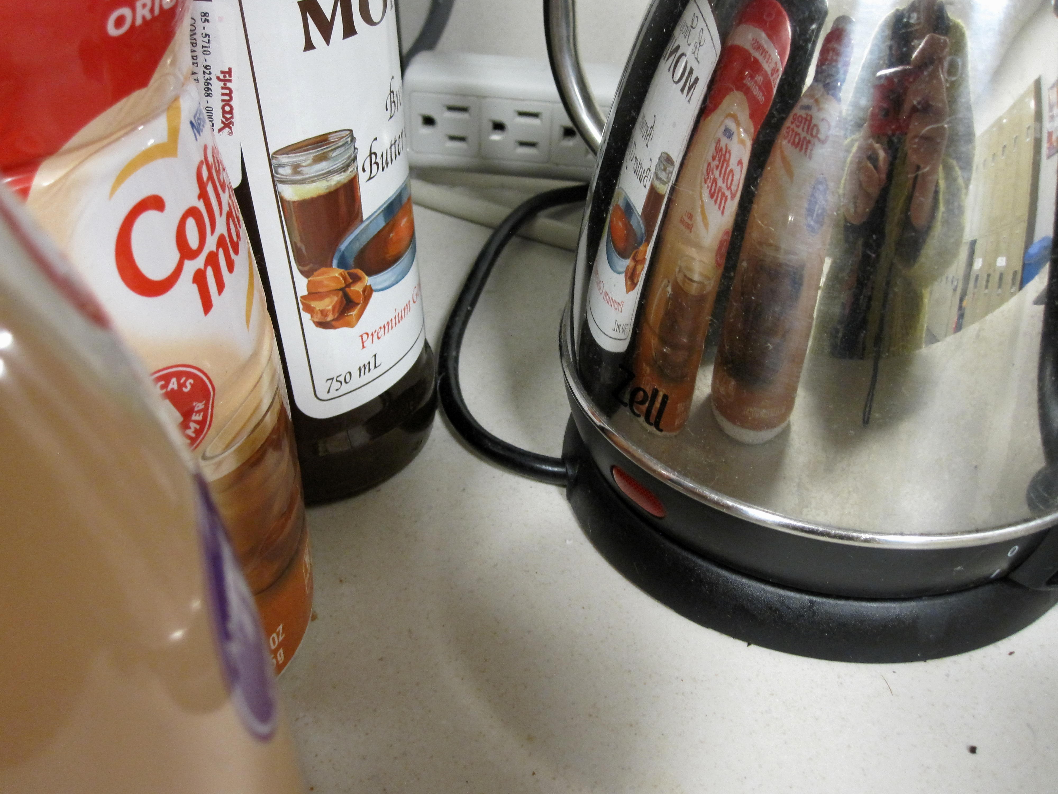 a group of flavored creamers sits next to a shiny kettle