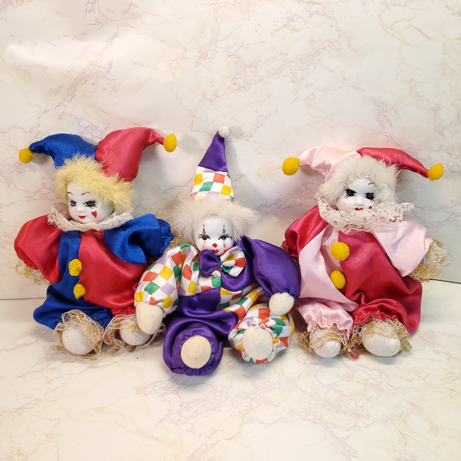 three porcelain-faced softbody clowns sit in a row
